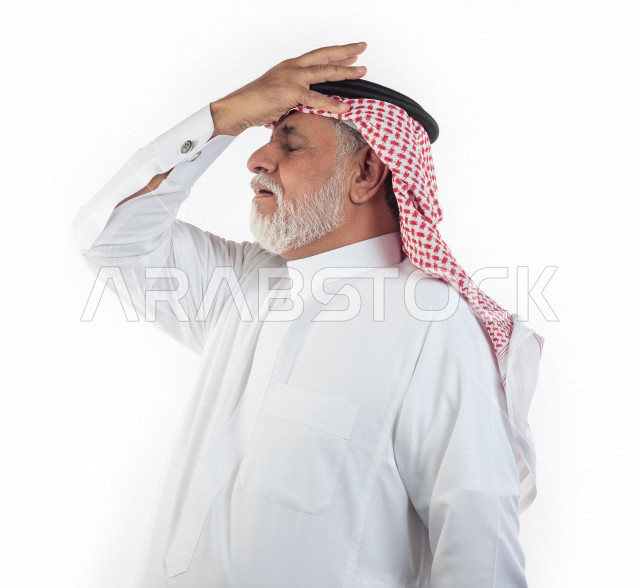 بورتريه رجل عربي سعودي كبير بالسن يضع يده على رأسه بإيماءات وجه ويدين مختلفة , صورة مقربة , شايب سعودي يرتدي ثوب أبيض مع شماغ وعقال , خلفية بيضاء , منظر جانبي لرجل مسن يضع يده على مقدمة رأسه في حالة من الصدمة والهم والحزن , مفهوم تعابيرالوجه ولغة الجسد ال