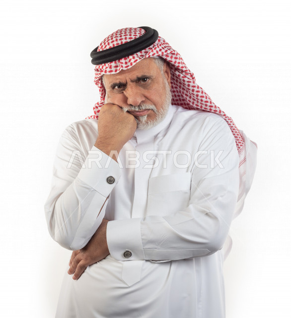 بورتريه رجل عربي سعودي كبير بالسن يضع يده على خده في حالة من الحزن والتعاسة , يرتدي ثوب أبيض مع شماغ وعقال , خلفية بيضاء , رجل مسن في حالة من التفكير العميق , مفهوم لغة الجسد وتعابيرالوجه