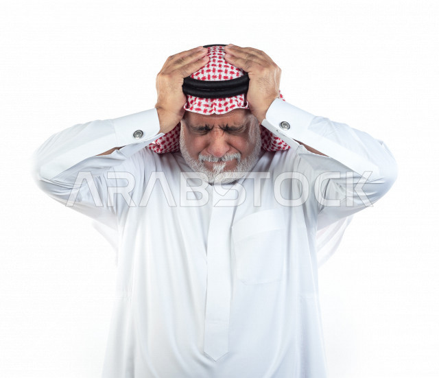 بورتريه رجل عربي سعودي كبير بالسن يضع يديه على رأسه يشعر بالألم والصداع , يرتدي ثوب أبيض مع شماغ وعقال , خلفية بيضاء , رجل مسن يتألم في رأسه , مفهوم لغة الجسد وتعابيرالوجه