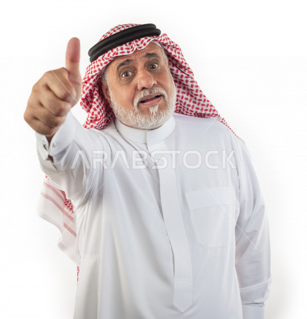 Portrait of an old Saudi Arab man pointing with his thumb in a stunned like sign, wearing a white dress with a shemagh and headband, white background, a stunned elderly man making a sign of approval with his thumb, the concept of body language and facial 