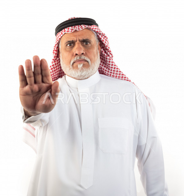 Portrait of an old Saudi Arab man pointing with his hand in anger, wearing a white dress with a shemagh and headband, white background, an angry elderly man pointing with his hand, the concept of body language and facial expression
