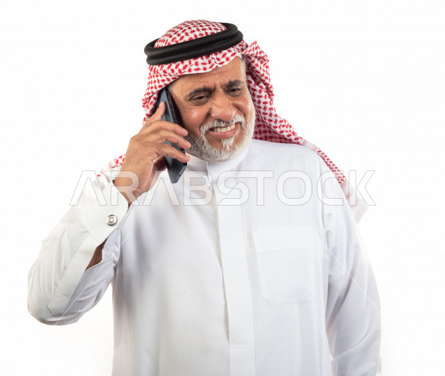 بورتريه رجل عربي سعودي كبير بالسن يتحدث على الجوال , يرتدي ثوب أبيض مع شماغ وعقال , خلفية بيضاء , رجل مسن يقوم بإجراء مكالمه والتواصل عبر الهاتف المحمول , مفهوم لغة الجسد وتعابيرالوجه
