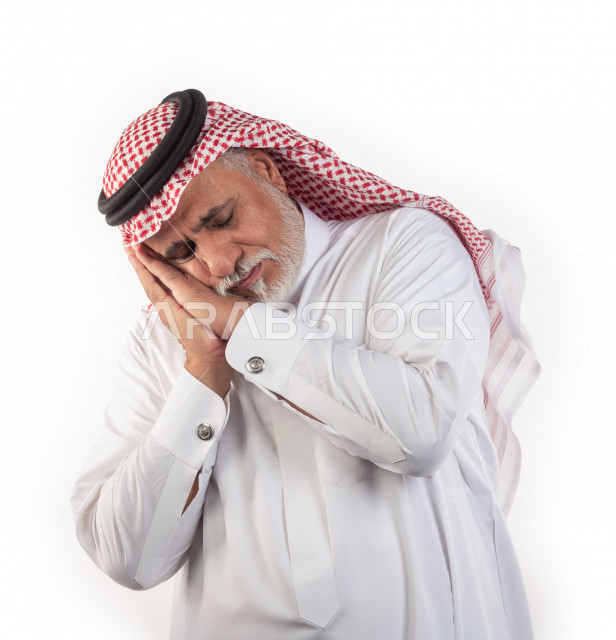 بورتريه رجل عربي سعودي كبير بالسن يضع رأسه على يديه للنوم وحالة من النعس , يرتدي ثوب أبيض مع شماغ وعقال , خلفية بيضاء , رجل مسن يلقي رأسه على اليدين للراحة مفهوم لغة الجسد وتعابير الوجه