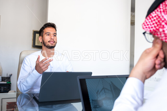 Collecting data and finding solutions to problems, using modern technical devices, cooperation, understanding and unity among team members, studying and developing new projects, workshops and business meetings at the company headquarters, a Saudi Gulf Arab businessman with an Emirati businessman discussing the project inside the office