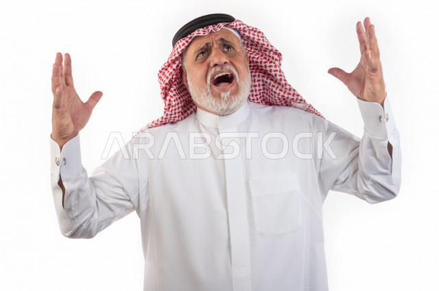 بورتريه رجل عربي سعودي كبير بالسن رافع اليدين يشعر بالقهر والإنزعاج النفسي , يرتدي ثوب أبيض مع شماغ وعقال , خلفية بيضاء , رجل مسن مقهور في حالة من الغضب والإنهيار , مفهوم لغة الجسد وتعابيرالوجه