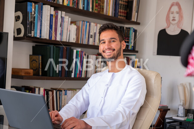 مهن ووظائف ادارية مكتبية, دمج العمل مع التقنيات والتكنولوجيا، إدارة شؤون الأعمال وتنظيمها عبر الاجهزة التقنية، رجل اعمال عربي خليجي اماراتي يرتدي الكندورة يعمل على الحاسوب المحمول داخل المكتب، إنجاز المهام العمل المطلوبة