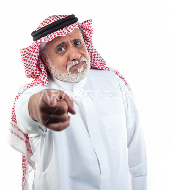 بورتريه رجل عربي سعودي كبير بالسن يشير بإصبعه بحالة من الحزن , يرتدي ثوب أبيض مع شماغ وعقال , خلفية بيضاء , رجل مسن حزين يشير بإصبعه مفهوم تعبير الوجه