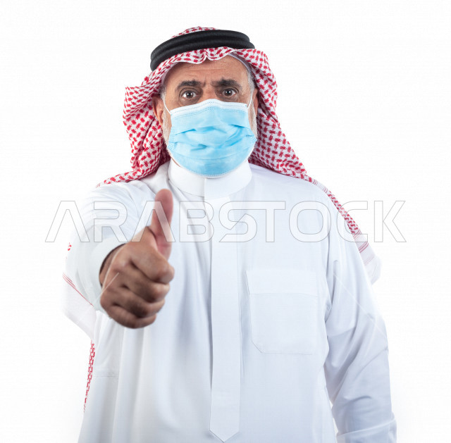 بورتريه رجل عربي سعودي كبير بالسن يشير بإصبعه مرتدي الكمامة , يرتدي ثوب أبيض مع شماغ وعقال , خلفية بيضاء , تعابير وجه و يدين مختلفة , الوقاية من كورونا (كوفيد-19)