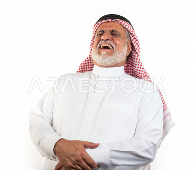 بورتريه رجل عربي سعودي كبير بالسن بإيدي متقاطعة وحالة من السعادة والفرح , يرتدي ثوب أبيض مع شماغ وعقال , خلفية بيضاء , رجل مسن يضحك ويبتسم مفهوم تعبيرالوجه 