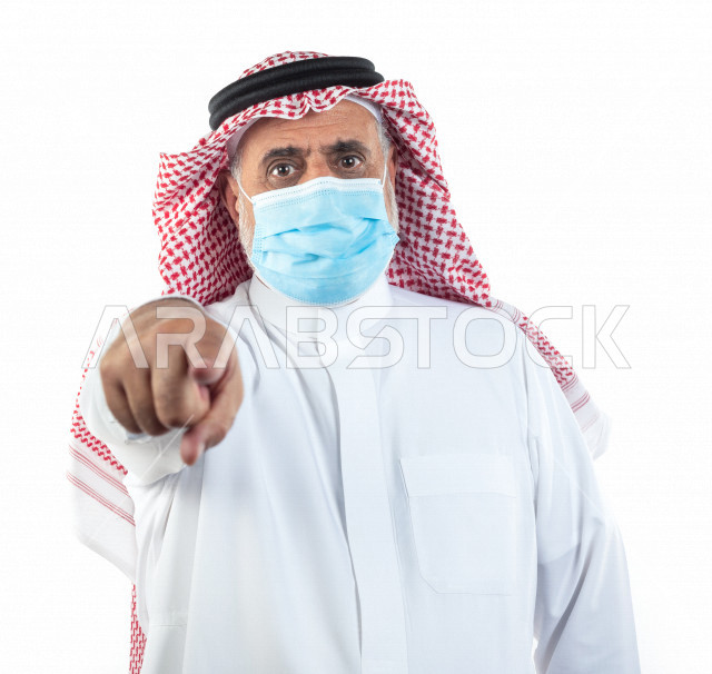 بورتريه رجل عربي سعودي كبير بالسن يشير بإصبعه مرتدي الكمامة , يرتدي ثوب أبيض مع شماغ وعقال , خلفية بيضاء , تعابير وجه و يدين مختلفة , الوقاية من كورونا (كوفيد-19)