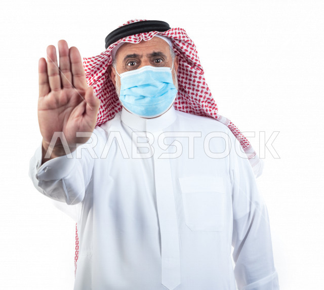 بورتريه رجل عربي سعودي كبير بالسن يشير بيده مرتدي الكمامة , يرتدي ثوب أبيض مع شماغ وعقال , خلفية بيضاء , تعابير وجه و يدين مختلفة , الوقاية من فايروس كورونا (كوفيد-19)