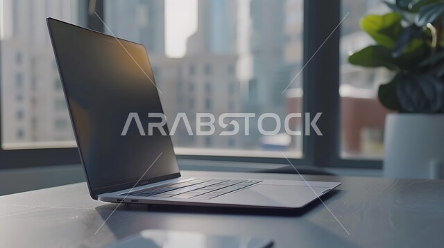 مكتب عمل بواجهه زجاجية كبيرة، طاولة عمل مجهزة باللوازم المكتبية، العمل على الحاسوب المحمول، استخدام الاجهزة التقنية الحديثة في المكاتب، مهن ووظائف ادارية، ديكورات وتصاميم وأثاث الغرفة الراقي