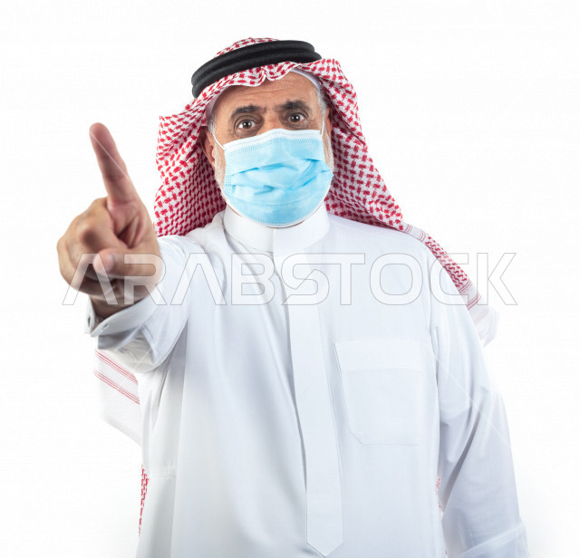بورتريه رجل عربي سعودي كبير بالسن يشير بإصبعه مرتدي الكمامة , يرتدي ثوب أبيض مع شماغ وعقال , خلفية بيضاء , تعابير وجه و يدين مختلفة , الوقاية من كورونا (كوفيد-19)