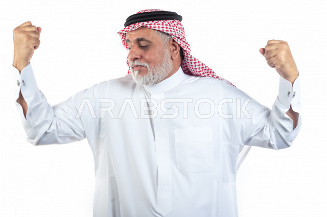 بورتريه رجل عربي سعودي كبير بالسن يقوم بحركة العضلات ذات الرأسين , يرتدي ثوب أبيض مع شماغ وعقال , خلفية بيضاء , رجل مسن ذو صحة بحركة العضلات ذات الرأسين وممارسة اللياقة البدنية مفهوم تعابيرالوجه ولغة الجسد المختلفة