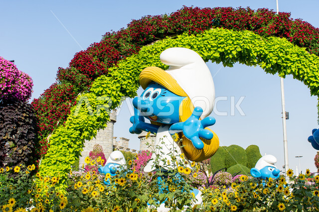 قضاء اوقات ممتعة في المناطق العامة, وجهات مثالية ترفيهية للأطفال, معالم سياحية مشهورة ,مجسم ثلاثي الابعاد لسنفورة باللون الازرق بين الاشجار داخل حديقة ميركل غاردن, الاهتمام في زراعة الازهار في قرية السنافر في دبي، الحدائق في الإمارات العربية المتحدة