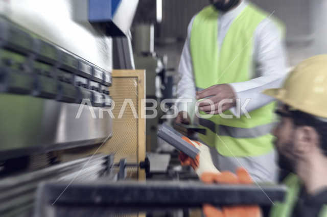 مهندسان  سعوديان عاملان يشرفان في داخل المصنع في المملكة العربية السعودية , إرتداء خوذة وسترة الحماية الخاصة بالعمل , العامل المسؤول بخوذة صفراء , المهندس المشرف بخوذة بيضاء , فحص المعدات بأنفسهم , تدقيق العمل , الإشراف والنقاش في العمل