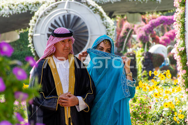 Interest in planting trees and flowers in gardens, distinguished agricultural engineering in the United Arab Emirates, famous recreational tourist attractions, spending enjoyable times in public parks, close-up of a couple of foreign tourists wearing traditional Arab dress in Miracle Garden