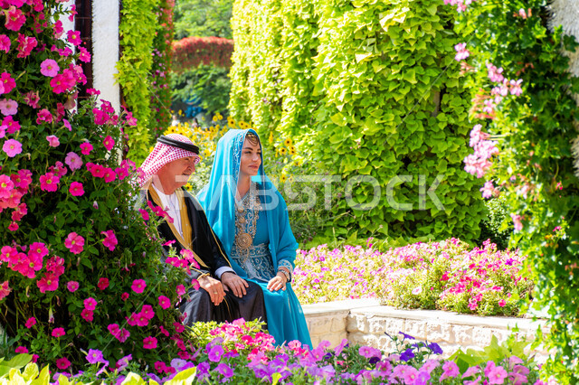 الهندسة الزراعية المتميزة في الإمارات العربية المتحدة، معالم سياحية ترفيهية مشهورة، قضاء اوقات ممتعة في الحدائق العامة، الاهتمام بزراعة الاشجار والورود في الحدائق، صورة من الجانب لزوجان من السياح الأجانب يرتدون الزي العربي التقليدي في حديقة ميركل غاردن