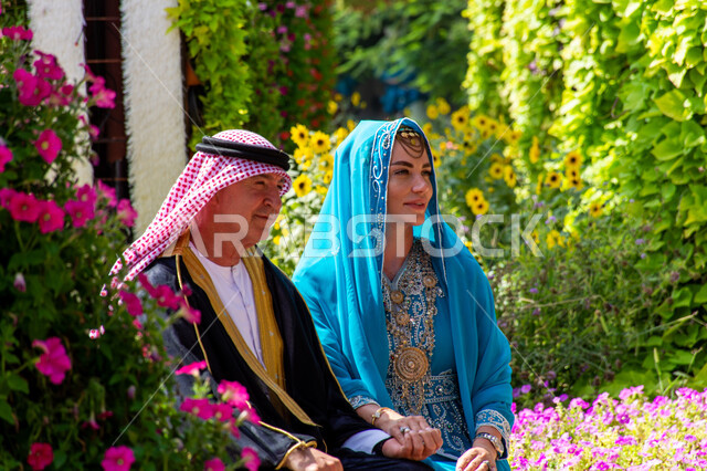 قضاء اوقات ممتعة في الحدائق العامة، الهندسة الزراعية المتميزة في الإمارات العربية المتحدة، معالم سياحية ترفيهية مشهورة، الاهتمام بزراعة الاشجار والورود في الحدائق، صورة مقربة من الجانب لزوجان من السياح الأجانب يرتدون الزي العربي التقليدي في حديقة ميركل غاردن