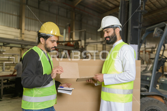 مهندسان  سعوديان عاملان يشرفان في داخل المصنع في المملكة العربية السعودية , إرتداء خوذة وسترة الحماية الخاصة بالعمل , العامل المسؤول بخوذة صفراء , المهندس المشرف بخوذة بيضاء , فحص المعدات بأنفسهم , تدقيق العمل , الإشراف والنقاش في العمل