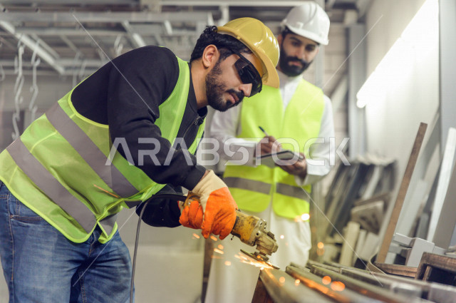 مهندسان  سعوديان عاملان يشرفان في داخل المصنع في المملكة العربية السعودية , إرتداء خوذة وسترة الحماية الخاصة بالعمل , العامل المسؤول بخوذة صفراء , المهندس المشرف بخوذة بيضاء , فحص المعدات بأنفسهم , تدقيق العمل , الإشراف والنقاش في العمل