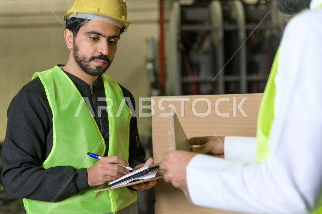 عامل مسؤول ومشرف سعودي يرتدي خوذه صفراء يشرف داخل المصنع في المملكة العربية السعودية , ارتداء خوذة وسترة الحماية الخاصة بالعمل , التصنيع والإشراف والتدقيق في العمل , الهندسة والصناعة