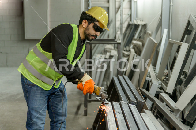 عامل مسؤول ومشرف سعودي يرتدي خوذه صفراء يشرف داخل المصنع في المملكة العربية السعودية , ارتداء خوذة وسترة الحماية الخاصة بالعمل , التصنيع والإشراف والتدقيق في العمل , الهندسة والصناعة