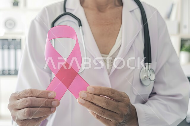 رمز الحملة العالمية، اليوم العالمي للتوعية بسرطان الثدي، صورة مقربة لطبيبة عربية خليجية سعودية ترتدي المعطف والسماعة الطبية تحمل بيدها شريط زهري اللون، الاهتمام بالمرض و بالكشف المبكر، الحملة التوعويه بالامراض الخبيثه