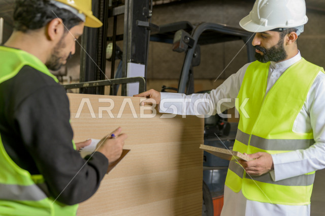 مهندسان  سعوديان عاملان يشرفان في داخل المصنع في المملكة العربية السعودية , إرتداء خوذة وسترة الحماية الخاصة بالعمل , العامل المسؤول بخوذة صفراء , المهندس المشرف بخوذة بيضاء , فحص المعدات بأنفسهم , تدقيق العمل , الإشراف والنقاش في العمل