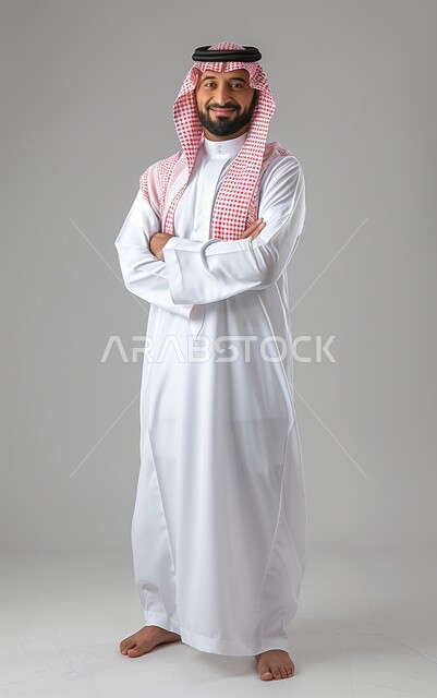 Looking at the camera with gestures of pleasure and self-confidence, interest in outward appearance, concept of elegance and masculinity, portrait of a smiling Saudi Arabian Gulf man wearing traditional thobe and shemagh standing with crossed hands, full body image, gray background.