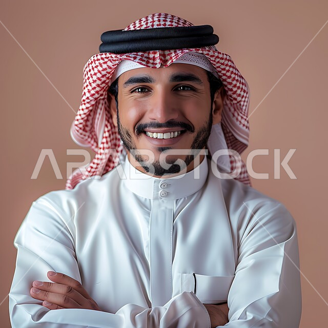 الوقوف بأيدي متقاطعة، التقاط صور شخصية للوثائق الرسمية، الأناقة والاهتمام بالمظهر الخارجي، مفهوم الوسامة والرجولة، بورتريه مقرب لرجل عربي خليجي سعودي مبتسم يرتدي الشماغ والثوب التقليدي ينظر الى الكاميرا بتعابير السرور والثقة بالنفس، خلفية وردية