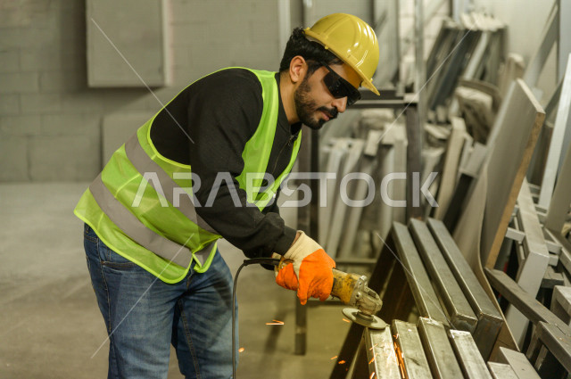 عامل مسؤول ومشرف سعودي يرتدي خوذه صفراء يشرف داخل المصنع في المملكة العربية السعودية , ارتداء خوذة وسترة الحماية الخاصة بالعمل , التصنيع والإشراف والتدقيق في العمل , الهندسة والصناعة