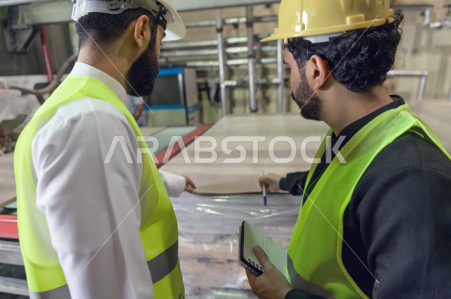 مهندسان  سعوديان عاملان يشرفان في داخل المصنع في المملكة العربية السعودية , إرتداء خوذة وسترة الحماية الخاصة بالعمل , العامل المسؤول بخوذة صفراء , المهندس المشرف بخوذة بيضاء , فحص المعدات بأنفسهم , تدقيق العمل , الإشراف والنقاش في العمل