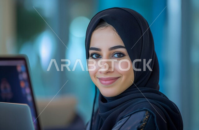 استخدام الأجهزة التكنولوجية الحديثة والمتطورة، الشركات والمكاتب في المملكة العربية السعودية، مهن ووظائف ادارية مكتبية, النظر إلى الكاميرا بإيماءات البهجة والسرور، إدارة شؤون الأعمال وتنظيمها، موظفة عربية خليجية سعودية محجبة تقوم بالعمل على الحاسوب داخل المكتب