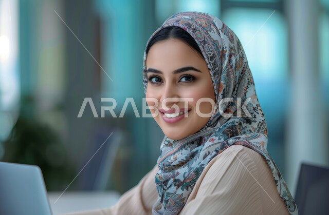 مهن ووظائف ادارية مكتبية, النظر إلى الكاميرا بإيماءات البهجة والسرور، استخدام الأجهزة التكنولوجية الحديثة والمتطورة، إدارة شؤون الأعمال وتنظيمها، موظفة عربية خليجية سعودية محجبة تقوم بالعمل على الحاسوب داخل المكتب، الشركات والمكاتب في المملكة العربية السعودية