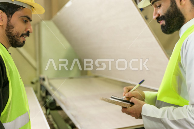 مهندسان  سعوديان عاملان يشرفان في داخل المصنع في المملكة العربية السعودية , إرتداء خوذة وسترة الحماية الخاصة بالعمل , العامل المسؤول بخوذة صفراء , المهندس المشرف بخوذة بيضاء , فحص المعدات بأنفسهم , تدقيق العمل , الإشراف والنقاش في العمل