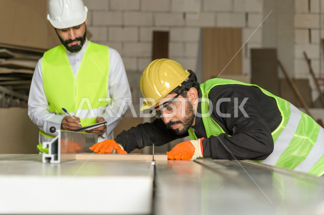 مهندسان  سعوديان عاملان يشرفان في داخل المصنع في المملكة العربية السعودية , إرتداء خوذة وسترة الحماية الخاصة بالعمل , العامل المسؤول بخوذة صفراء , المهندس المشرف بخوذة بيضاء , فحص المعدات بأنفسهم , تدقيق العمل , الإشراف والنقاش في العمل
