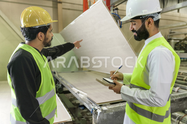 مهندسان  سعوديان عاملان يشرفان في داخل المصنع في المملكة العربية السعودية , إرتداء خوذة وسترة الحماية الخاصة بالعمل , العامل المسؤول بخوذة صفراء , المهندس المشرف بخوذة بيضاء , فحص المعدات بأنفسهم , تدقيق العمل , الإشراف والنقاش في العمل