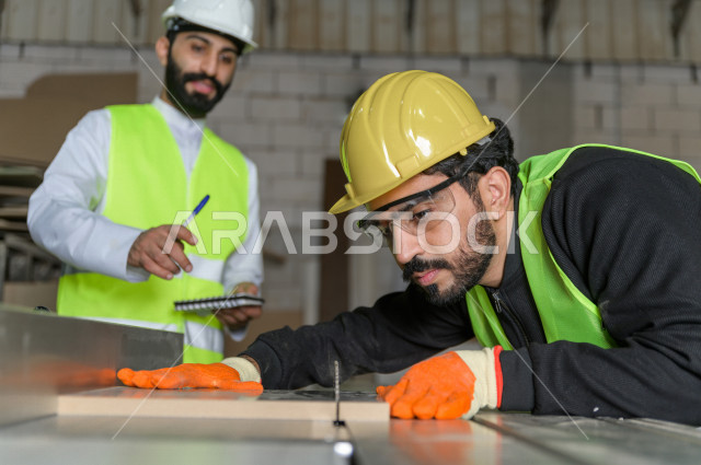 مهندسان  سعوديان عاملان يشرفان في داخل المصنع في المملكة العربية السعودية , إرتداء خوذة وسترة الحماية الخاصة بالعمل , العامل المسؤول بخوذة صفراء , المهندس المشرف بخوذة بيضاء , فحص المعدات بأنفسهم , تدقيق العمل , الإشراف والنقاش في العمل