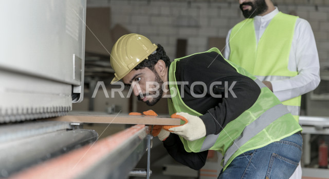 مهندسان  سعوديان عاملان يشرفان في داخل المصنع في المملكة العربية السعودية , إرتداء خوذة وسترة الحماية الخاصة بالعمل , العامل المسؤول بخوذة صفراء , المهندس المشرف بخوذة بيضاء , فحص المعدات بأنفسهم , تدقيق العمل , الإشراف والنقاش في العمل