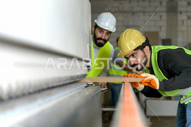 مهندسان  سعوديان عاملان يشرفان في داخل المصنع في المملكة العربية السعودية , إرتداء خوذة وسترة الحماية الخاصة بالعمل , العامل المسؤول بخوذة صفراء , المهندس المشرف بخوذة بيضاء , فحص المعدات بأنفسهم , تدقيق العمل , الإشراف والنقاش في العمل