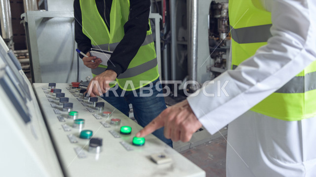 صورة مقربة ليد المهندسان السعوديان العاملان يقومون بالإشراف في داخل المصنع في المملكة العربية السعودية , إرتداء سترة الحماية الخاصة بالعمل , فحص المعدات بأنفسهم , تدقيق العمل , الإشراف والنقاش في العمل , لوحة أزرار التحكم , كيفية آلية التشغيل في المصنع