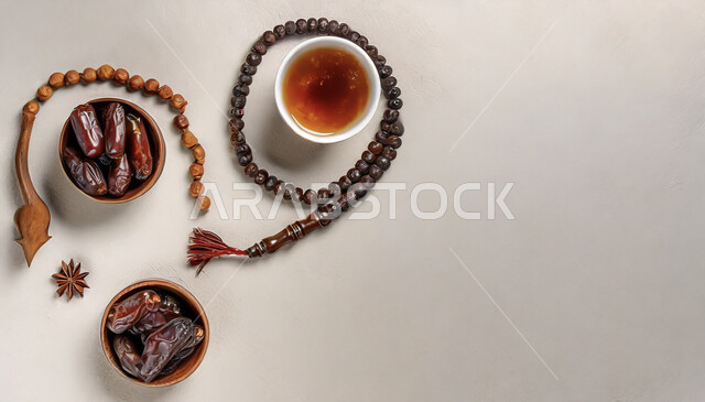 Rosary made of beads for the remembrance of Allah Almighty, commitment and adherence to remembrance, hospitality of occasions and holidays in the Kingdom of Saudi Arabia, vertical top view of a bowl full of dates next to a cup of red tea, local national products and crops, white background