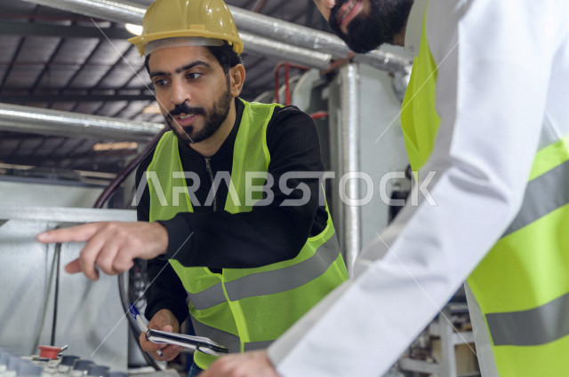 مهندسان  سعوديان عاملان يشرفان في داخل المصنع في المملكة العربية السعودية , إرتداء خوذة وسترة الحماية الخاصة بالعمل , العامل المسؤول بخوذة صفراء , المهندس المشرف بخوذة بيضاء , فحص المعدات بأنفسهم , تدقيق العمل , الإشراف والنقاش في العمل