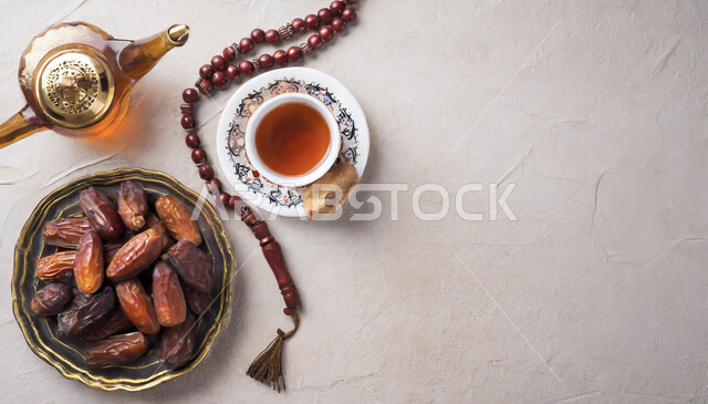 سبحه مصنوعه من الخرز لذكر الله تعالى, الالتزام والتمسك بالذكر، ضيافة المناسبات والأعياد في المملكة العربية السعودية, صورة علوية عامودية ل وعاء مليء بالتمر بجانب كوب الشاي الأحمر، منتجات ومحاصيل وطنية محلية، خلفية بيضاء