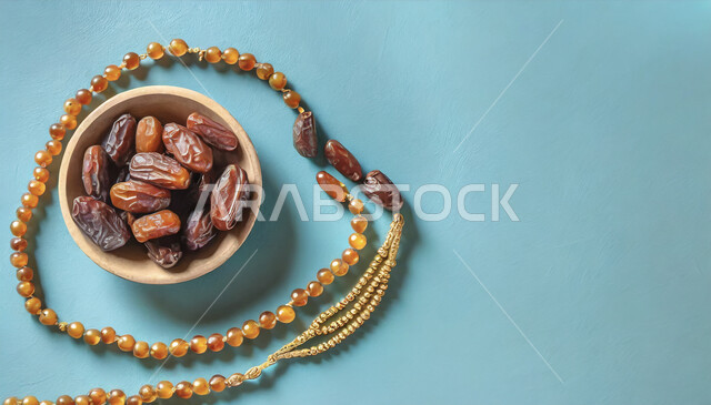 الالتزام والتمسك بالأذكار، ضيافة المناسبات والأعياد في المملكة العربية السعودية, صورة علوية عامودية ل وعاء مليء بالتمر بجانب سبحه مصنوعه من الخرز لذكر الله تعالى، منتجات ومحاصيل وطنية محلية، خلفية زرقاء