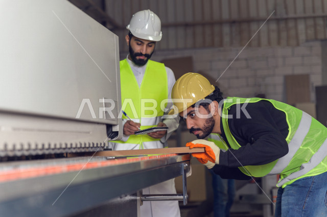 مهندسان  سعوديان عاملان يشرفان في داخل المصنع في المملكة العربية السعودية , إرتداء خوذة وسترة الحماية الخاصة بالعمل , العامل المسؤول بخوذة صفراء , المهندس المشرف بخوذة بيضاء , فحص المعدات بأنفسهم , تدقيق العمل , الإشراف والنقاش في العمل