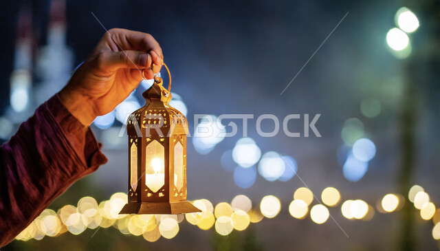 إضاءة وزينة شهر رمضان المبارك، فوانيس وتحف اسلامية للاحتفال بقدوم شهر الخير، صورة مقربة لأيدي رجل عربي خليجي سعودي يحمل فانوس معدني مضيء، ديكورات وأنوار في الأجواء الرمضانية الروحانية