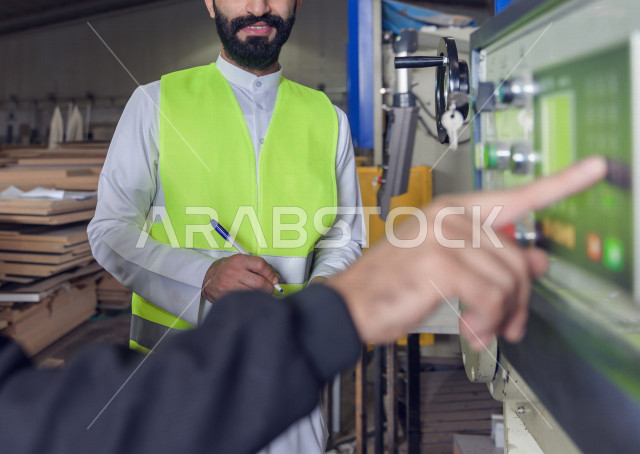 مهندسان  سعوديان عاملان يشرفان في داخل المصنع في المملكة العربية السعودية , إرتداء خوذة وسترة الحماية الخاصة بالعمل , العامل المسؤول بخوذة صفراء , المهندس المشرف بخوذة بيضاء , فحص المعدات بأنفسهم , تدقيق العمل , الإشراف والنقاش في العمل