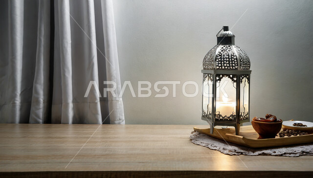 ديكورات وأنوار في الأجواء الرمضانية الروحانية، صورة مقربة لفانوس معدني مزخرف مضيء على طاولة خشبية، تحف اسلامية تقليدية للاحتفال بقدوم شهر الخير، زينة رمضان المبارك على الطراز الاسلامي